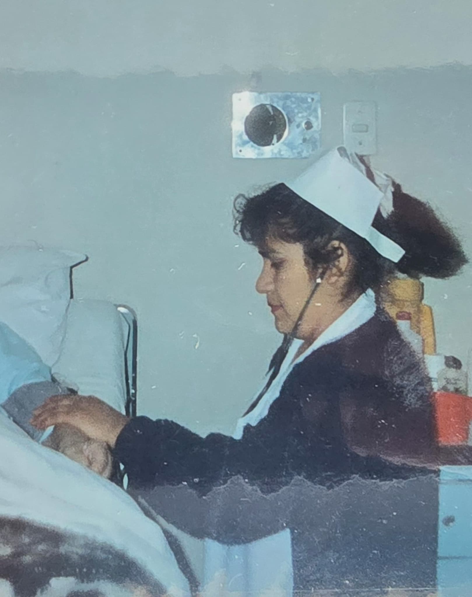 An old photograph of Justina in a nurse's uniform and cap, caring for a patient during her years working in healthcare.