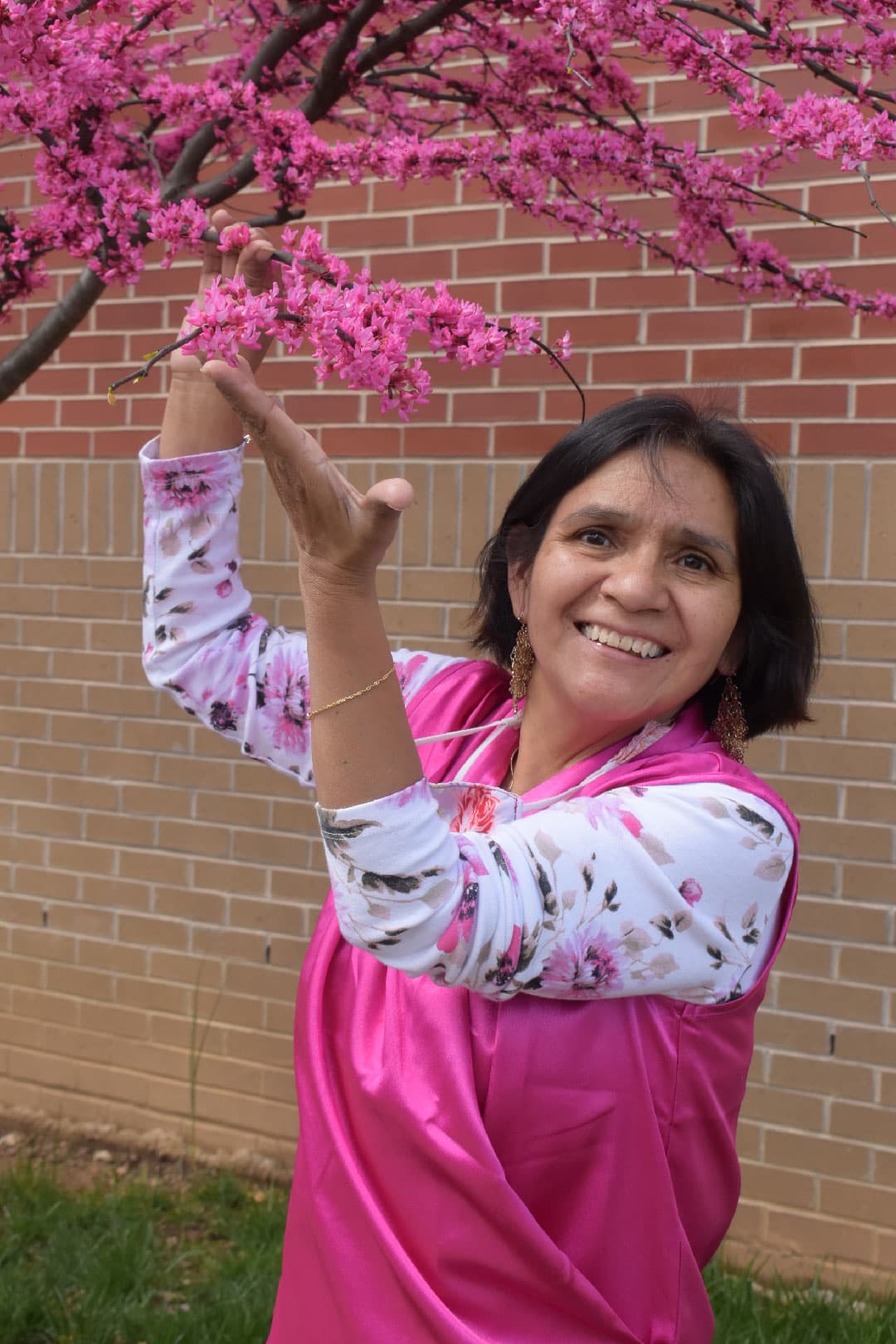 Justina Tiburcio-Brown, who owns and runs Kids Club Home DayCare, smiling as she reaches up to a branch of pink blossom.