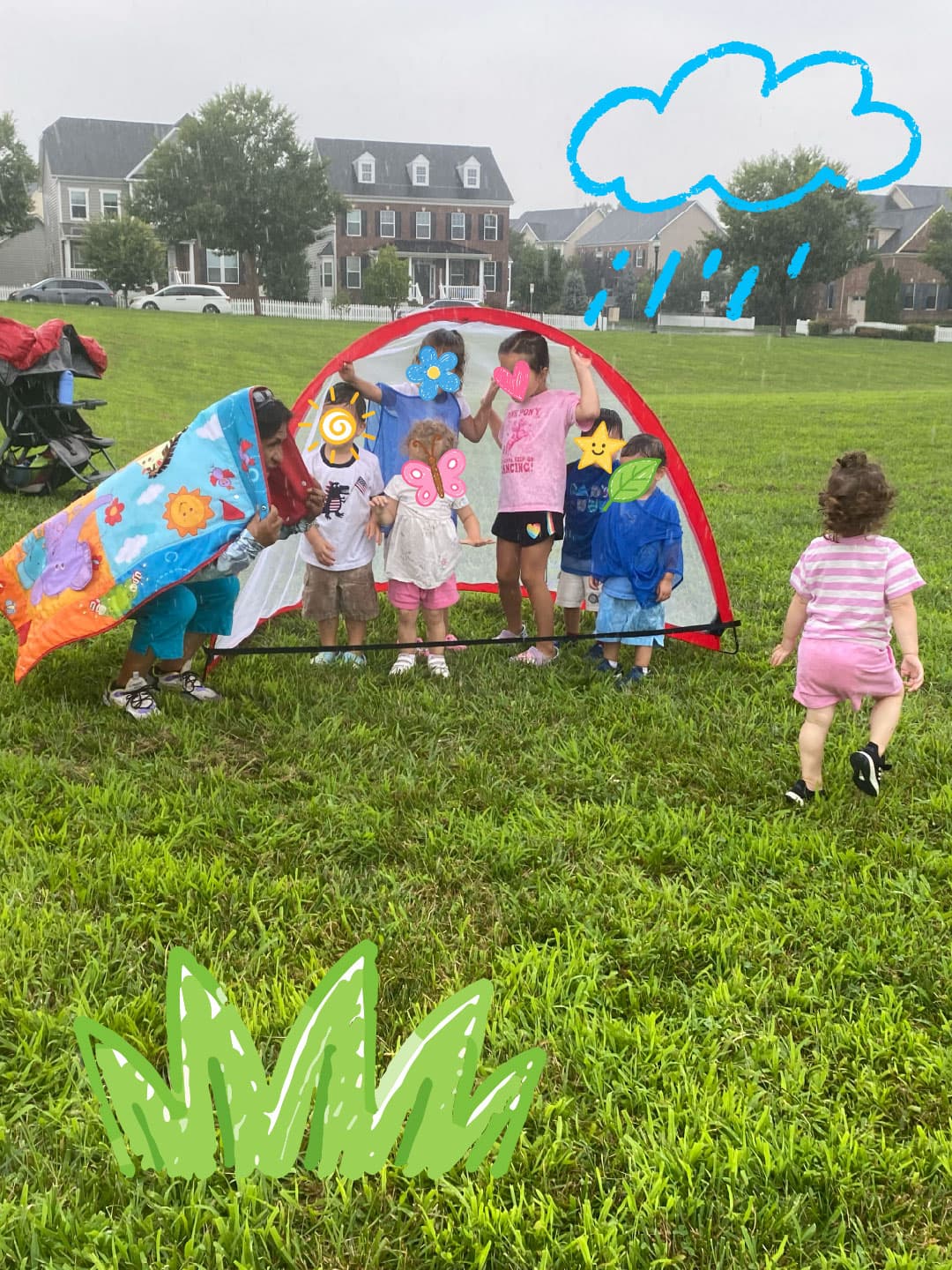 Children sheltering under a pop-up play tent on the grass in light rain, with one toddler walking over to join them.