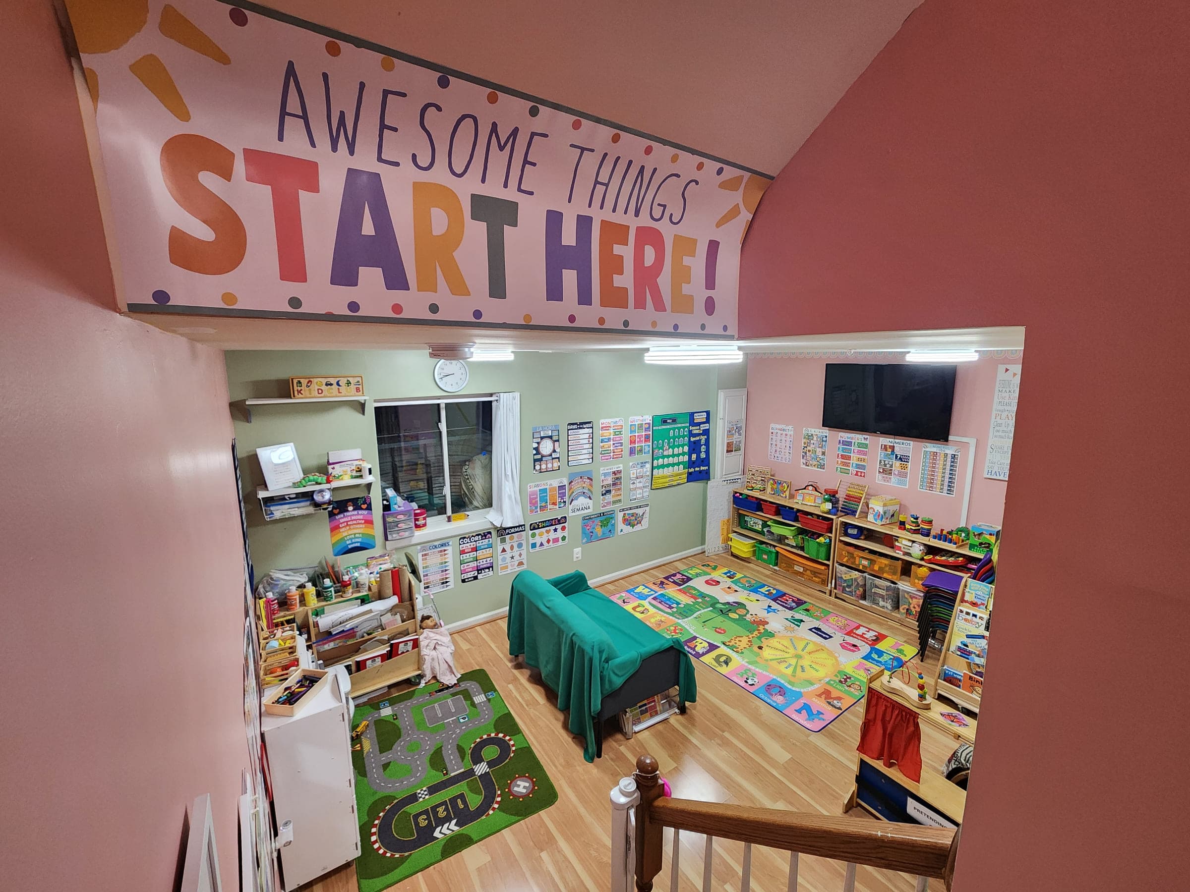 The main playroom at Kids Club Home DayCare, with shelves of toys and books, a low table, a road-map rug and learning charts on the walls, under a banner reading Awesome Things Start Here.